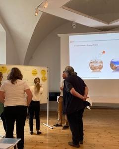 Mehrere personen stehen vor einer großen Tafel und befestigen gelbe Zettel mit Magneten darauf.