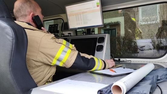 Ein Feuerwehrmann am Leitstellentisch, mit Telefonhörer am Ohr und Hand an der Maus seines Computers