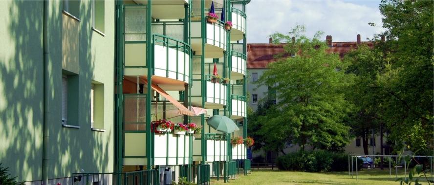 mehrstöckiger Wohnblock mit Balkonen und einer Wiese mit Bäumen davor