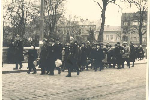 Alte schwarz-weiß-Aufnahme mit einer großen Menschengruppe in Winterkleidung, vornweg Polizisten