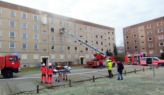 Einsatzgeschehen der Feuerwehr vor einem Wohnblock, aus einem Fenster kommt Rauch