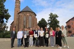 Gruppenbild der Ausbildungs- und Verwaltungsleitung mit den neuen Azubis und Studierenden vor der Johanniskirche. ,