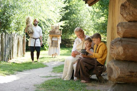 Als Slawen verkleidete Familie sitzt vor einem historischem Nachbau einer Slawenhütte aus Holz