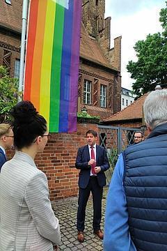 OB Steffen Scheller redet vor einer Menschengruppe, im Hintergrund die Regenbogenflagge