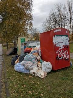 viele Altkleider liegen neben dem Altkleidercontainer