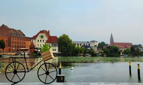 Miniatur-Fahrrad im Vordergrund, im Hintergrund Wasser und Häuserfronten am Wasser sowie der Dom zu Brandenburg