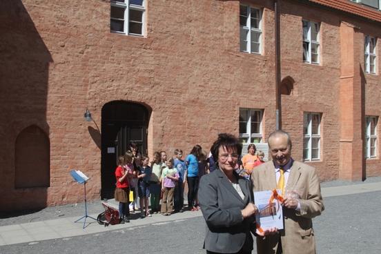 Hannelore Klabunde überreicht Dr. Martin Martiny die Urkunde. Im Hintergrund ist das ausgezeichnete Gebäude Burghof 6 zu sehen.
