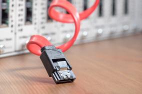 Symbolbild eines Webservers: Server unscharf im Hintergrund und ein rotes Verbindunskabel im Vordergrund