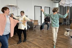 Drei Frauen balancieren mit einem Spitzenregenschirm auf einer Linie am Boden
