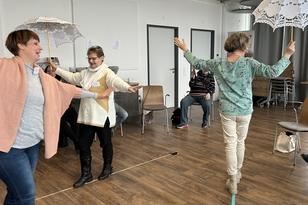 Drei Frauen balancieren mit einem Spitzenregenschirm auf einer Linie am Boden