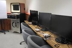 Computerkabinett mit stühlen und Bildschirmen die nebeneinander angeordnet sind.