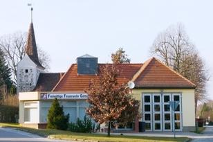 Feuerwehrwache mit Tor für Einsatzwagen und Kirchengebäude im Hintergrund