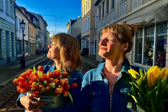 Zwei Frauen genießen die Sonnenstrahlen und halten Tulpen in großen Töpfen in den Händen.