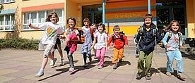 Kinder laufen lachend aus einem Schulgebäude heraus