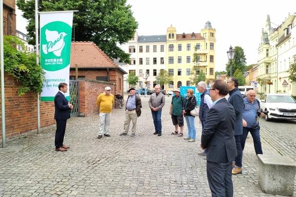 OB Stellen Scheller steht im Kreis weiterer Personen, hinter ihm die Flagge für Mayors 4 Peace