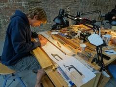 Ein Mann sitzt an einer Werkbank und zeichnet auf Papier.