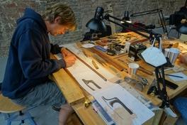 Ein Mann sitzt an einer Werkbank und zeichnet auf Papier.