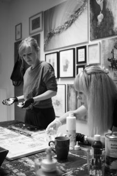 Schwarz-Weiß-Aufnahme von zwei Frauen mit Handschuhen an den Händen und Farbe an den Handschuhen