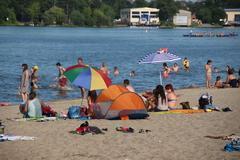Menschen in Badekleidung und mit Sonnenschirmen am Stand, dahinter Wasser