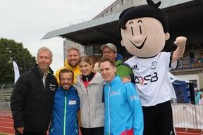 mehrere Sportler lassen sich fotografieren mit dem DOSB Maskottchen.