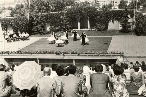 Veranstaltung auf der Freilichtbühne. Die Freilichtbühne ist von hinteren Plätzen aus zu sehen. Im Hintergrund tanzen Paare auf der Bühne, im Vordergrund sind die Rücken der Zuschauer zu erkennen.