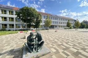 Schulgebäude mit Skulptur mit zwei Schülern.