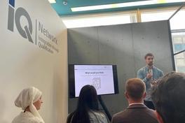 Hinterköpfe von vier Personen die einen Mann anschauen der gerade einen Vortrag hält. 