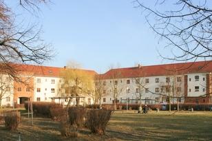 Dreistöckiger Wohnblock mit Spitzdach mit einer großen Wiese im Vordergrund
