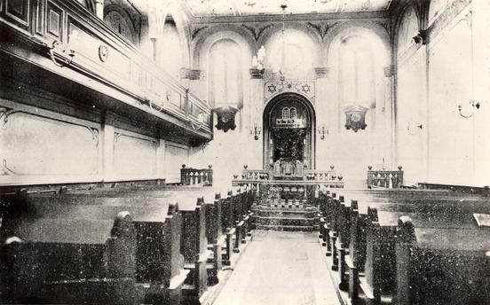 Schwarz-Weiß-Aufnahme vom Innenraum der Synagoge, mit Holzbänken, Emporen, Tora-Schrein und großen Fenstern
