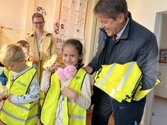 Oberbürgermeister Steffen Scheller hilft einer Schülerin bei der Anprobe der Sicherheitswarnweste.