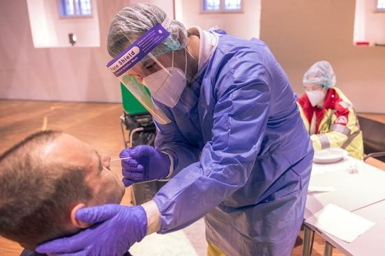 Eine Person in medinizischer Schutzausrüstung nimmt einen Corona-Nasentest bei einem sitzenden Mann vor