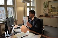 Steffen Scheller sitzt an seinem Arbeitsplatz vor dem Computer und hält einen Zettel (den Fördermittelscheck) in die Webcam