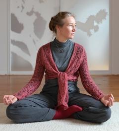 Eine Frau sitzt im Schneidersitzt auf einer Matte