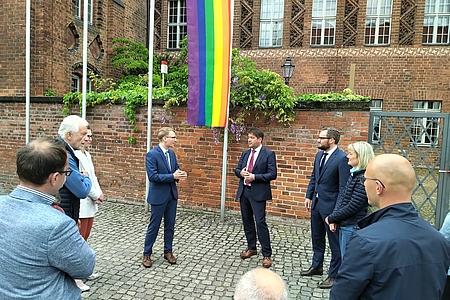 Personengruppe steht vor der Regenbogenflagge vor dem Rathaus