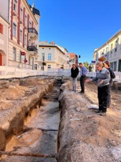 Die Grabungsleiterin steht mit 3 weiteren Personen rechts von dem 1,30 Meter breiten Graben.
