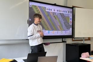 Ein Schüler steht vor der Klasse neben einem Smart Board und präsentiert seinen Straßenentwurf.