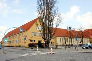 2-stöckiges Schulgebäude mit einem Fußgängerüberweg und einem Parkplatz im Vordergrund