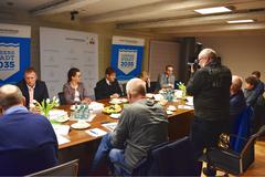 mehrere Personen sitzen an einem Tisch, auf der einen Seite der OB und die Beigeordneten, auf der anderen Seite Pressevertreter