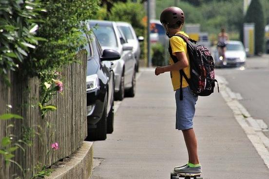 Junge auf einem Skateboard mit Helm und Rucksack auf dem Rücken auf einer Straße.
