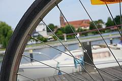 im Vordergrund die Speichen und der Reifen eines Fahrrads, im Hintergrund Wasser, ein Boot und der Brandenburger Dom