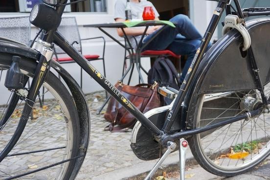 Fahrrad steht am Wegesrand, dahinter sitzt jemand entspannt an einem Café-Tisch
