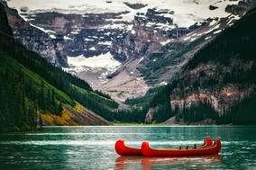 ein rotes Kanu auf einem blauen See, dahinter schneebedeckte Berge
