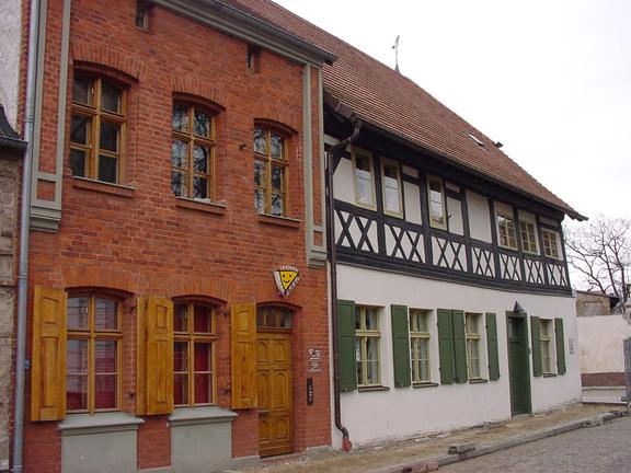 Rotes Backsteingebäude mit Logo der Galerie über der Tür, angrenzend an ein Fachwerkhaus