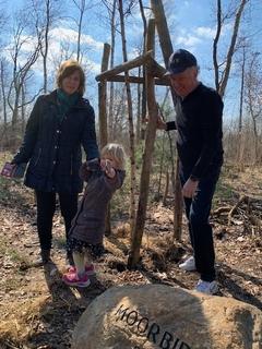 Ein Mann, eine Frau und ein Kleinkind stehen neben der Birke und lachen in die Kamera, daneben ein Stein mit der Aufschrift "Moorbirke 2023"