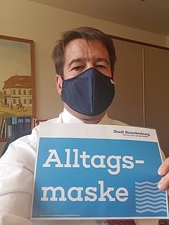 Selfie von Steffen Scheller, der eine Maske trägt und das Schild "Alltagsmaske" in der Hand hält