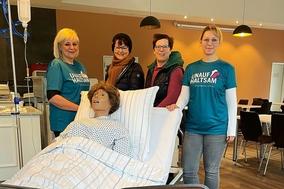 Pflegekräfte und Gäste stehen an einem Bett mit Puppe im Asklepios Fachklinikum