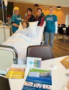 Pflegekräfte und Gäste stehen an einem Bett mit Puppe im Asklepios Fachklinikum