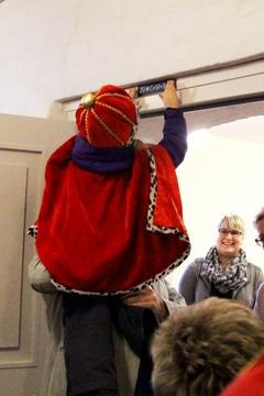 ein Kind auf den Schultern eines Erwachsenen bringt ein kleines Schild über einer Tür an