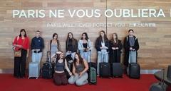 9 Schüler und eine Lehrerin am Flughafen Paris vor einem Schild mit der Aufschrift "Paris wird dich nie vergessen"