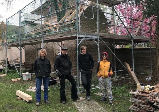 4 Personen stehen vor einem kleinen Haus mit Baugerüst